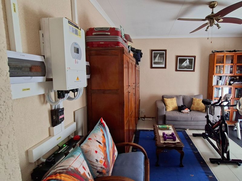 A living room area featuring a ceiling fan, tiled flooring, and a wall-mounted inverter system with an electrical distribution board.