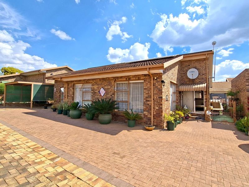 Front elevation of a facebrick townhouse featuring a paved driveway, tiled roof, and secure entrance area.