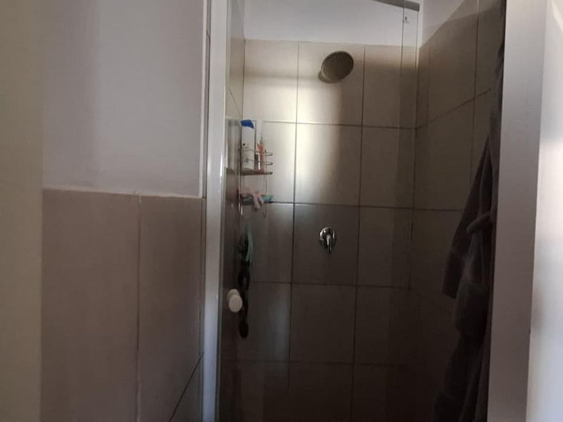 A functional shower enclosure featuring tiled walls, a fixed shower head, and a glass screen.