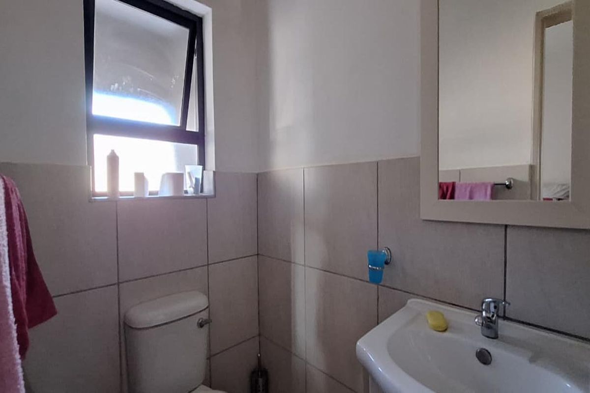 A functional bathroom featuring tiled walls, a pedestal basin, a framed mirror, and a top-hung window for natural ventilation.