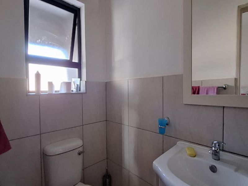 A functional bathroom featuring tiled walls, a pedestal basin, a framed mirror, and a top-hung window for natural ventilation.