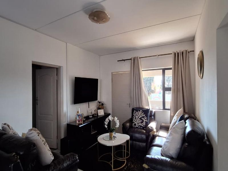 A compact living room featuring neutral walls, a central ceiling light, and access to adjacent rooms via internal doors.