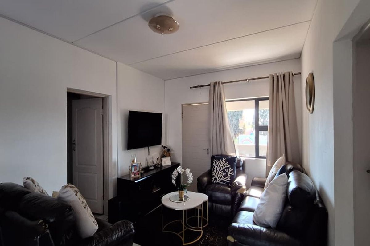 A compact living room featuring neutral walls, a central ceiling light, and access to adjacent rooms via internal doors.