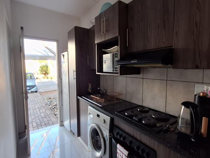 Compact kitchen featuring dark wood cabinetry, granite countertops, built-in electric hob, extractor fan, and tiled flooring with direct access to the exterior.