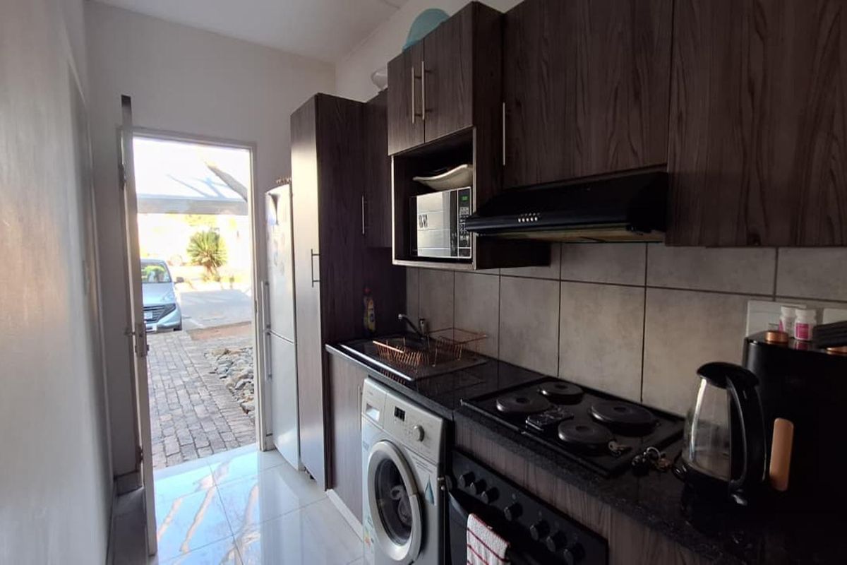 Compact kitchen featuring dark wood cabinetry, granite countertops, built-in electric hob, extractor fan, and tiled flooring with direct access to the exterior.