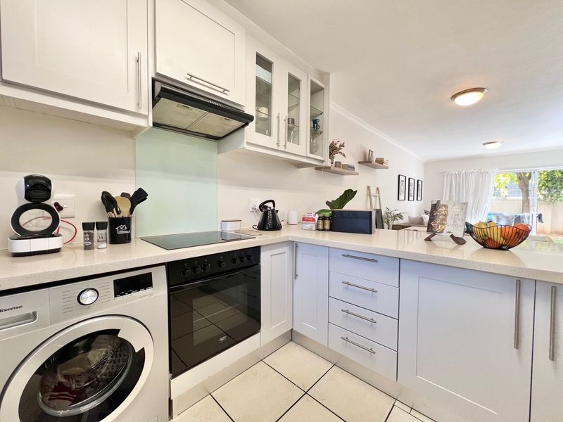 A well-maintained kitchen featuring white cabinetry, stone countertops, integrated appliances, and a glass splashback, flowing into an open-plan living area.