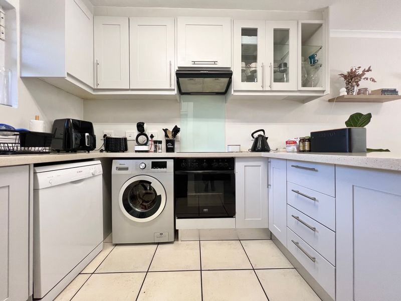 A well-maintained kitchen featuring white cabinetry, integrated oven, extractor fan, glass splashback, and tiled flooring with ample counter space.