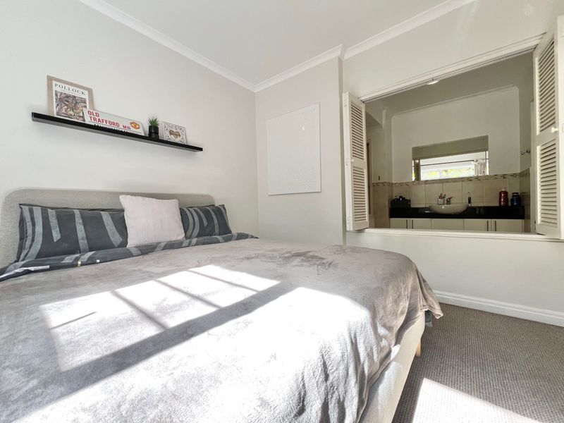 A well-maintained bedroom featuring neutral walls, carpeted flooring, and a unique internal shutter window providing a view into the adjoining bathroom.