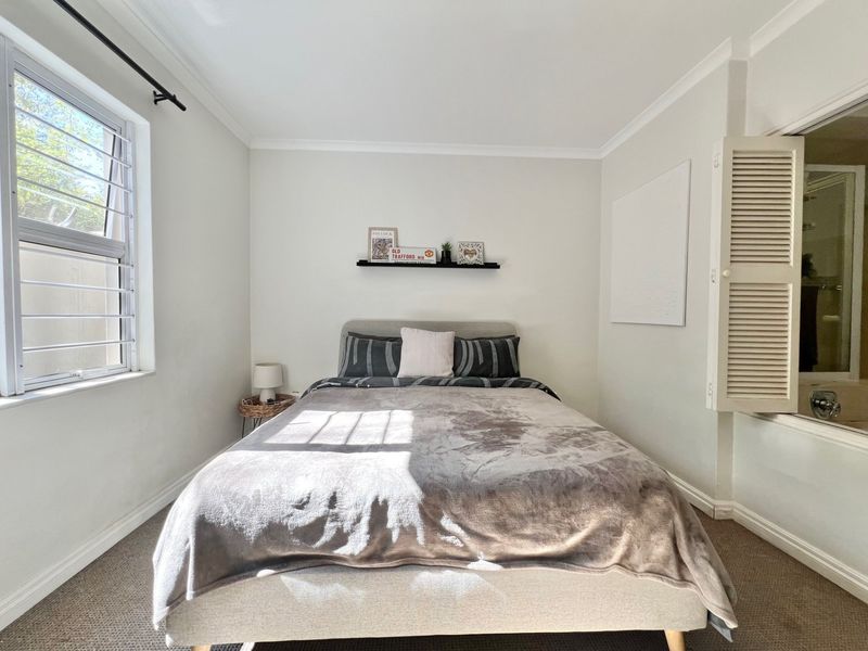 A well-maintained bedroom featuring carpeted flooring, security bars on the window, and louvered shutters opening into an adjacent bathroom.