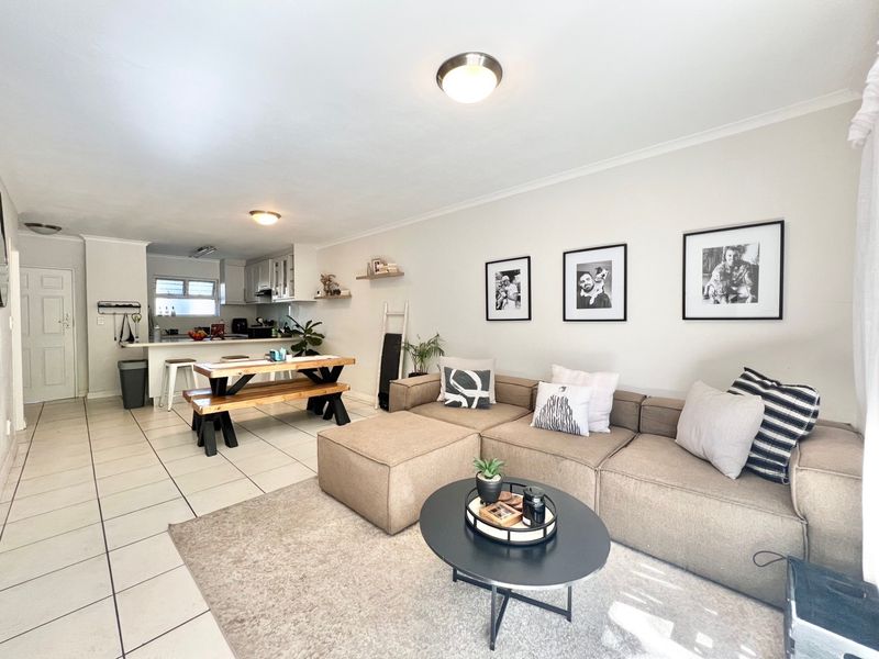 An open-plan living and kitchen area featuring tiled flooring, neutral walls, and functional cabinetry, creating a bright and cohesive living space.