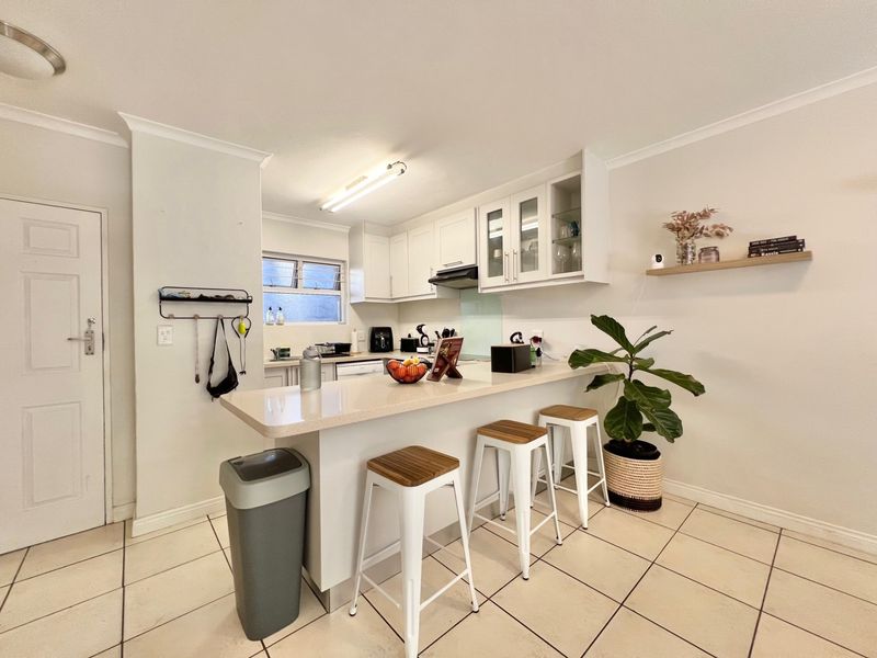 A functional kitchen featuring white cabinetry, stone countertops, a breakfast bar, and tiled flooring, offering a clean and practical layout for daily use.