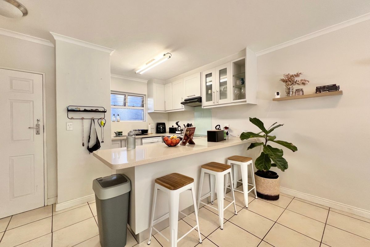 A functional kitchen featuring white cabinetry, stone countertops, a breakfast bar, and tiled flooring, offering a clean and practical layout for daily use.