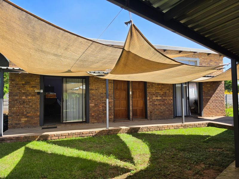 A covered patio area featuring face brick walls, shade sails, and multiple access points through sliding glass and timber doors overlooking a garden.