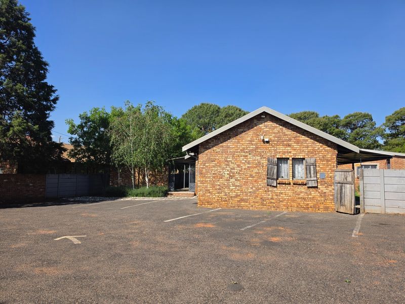 Front exterior view of a face brick guest house building featuring a paved parking area and secure boundary walling.