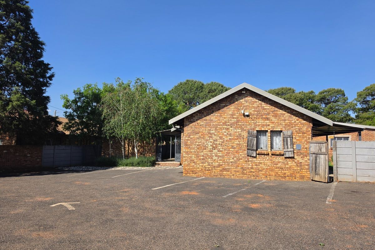 Front exterior view of a face brick guest house building featuring a paved parking area and secure boundary walling.