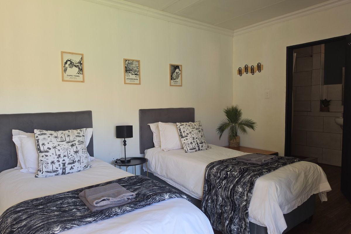 A well-maintained bedroom featuring laminate flooring, crown molding, and an en-suite bathroom entrance, offering a clean and functional guest accommodation space.