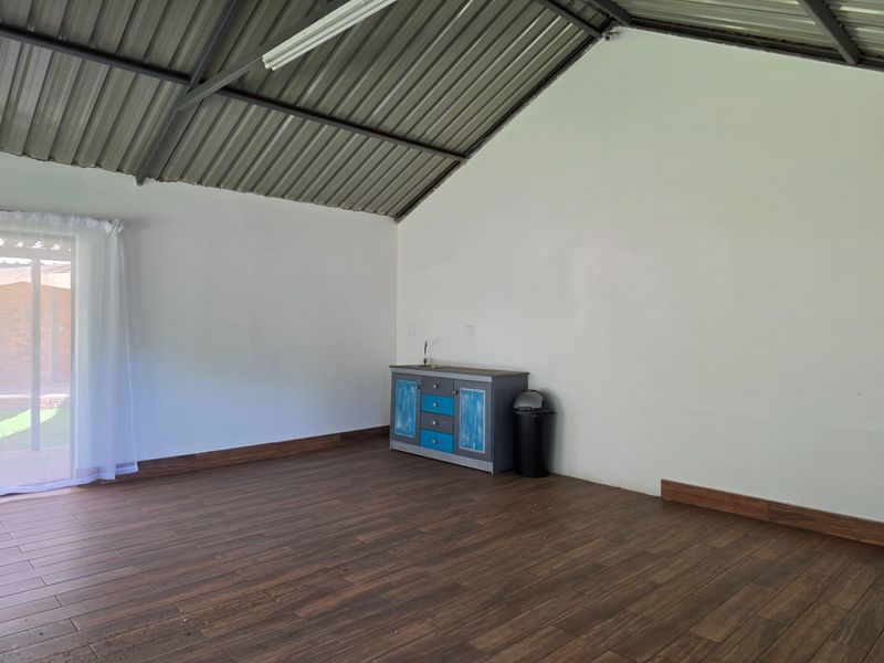 An open-plan space featuring wood-look tile flooring, exposed metal roof structure, and a small built-in vanity unit with a sink.