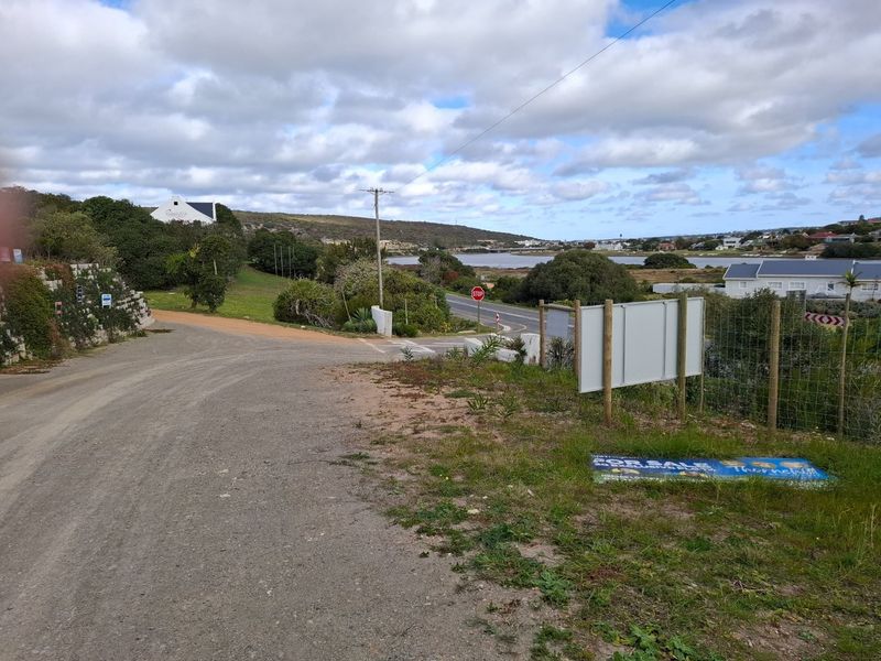 A view of the access road and surrounding landscape, featuring a gravel path, utility infrastructure, and nearby residential development.