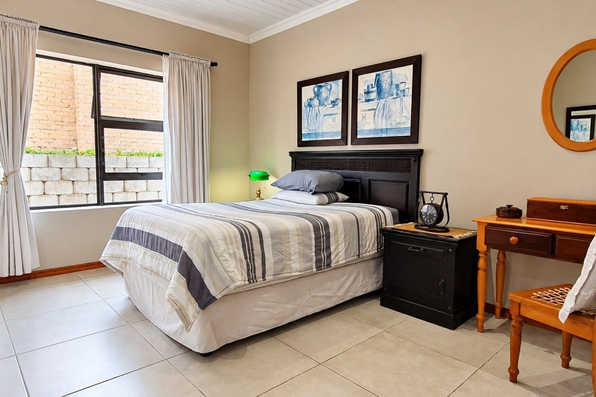 A well-maintained bedroom featuring neutral tiled flooring, large aluminium-framed windows, and classic cornice detailing, offering a clean and functional living space.