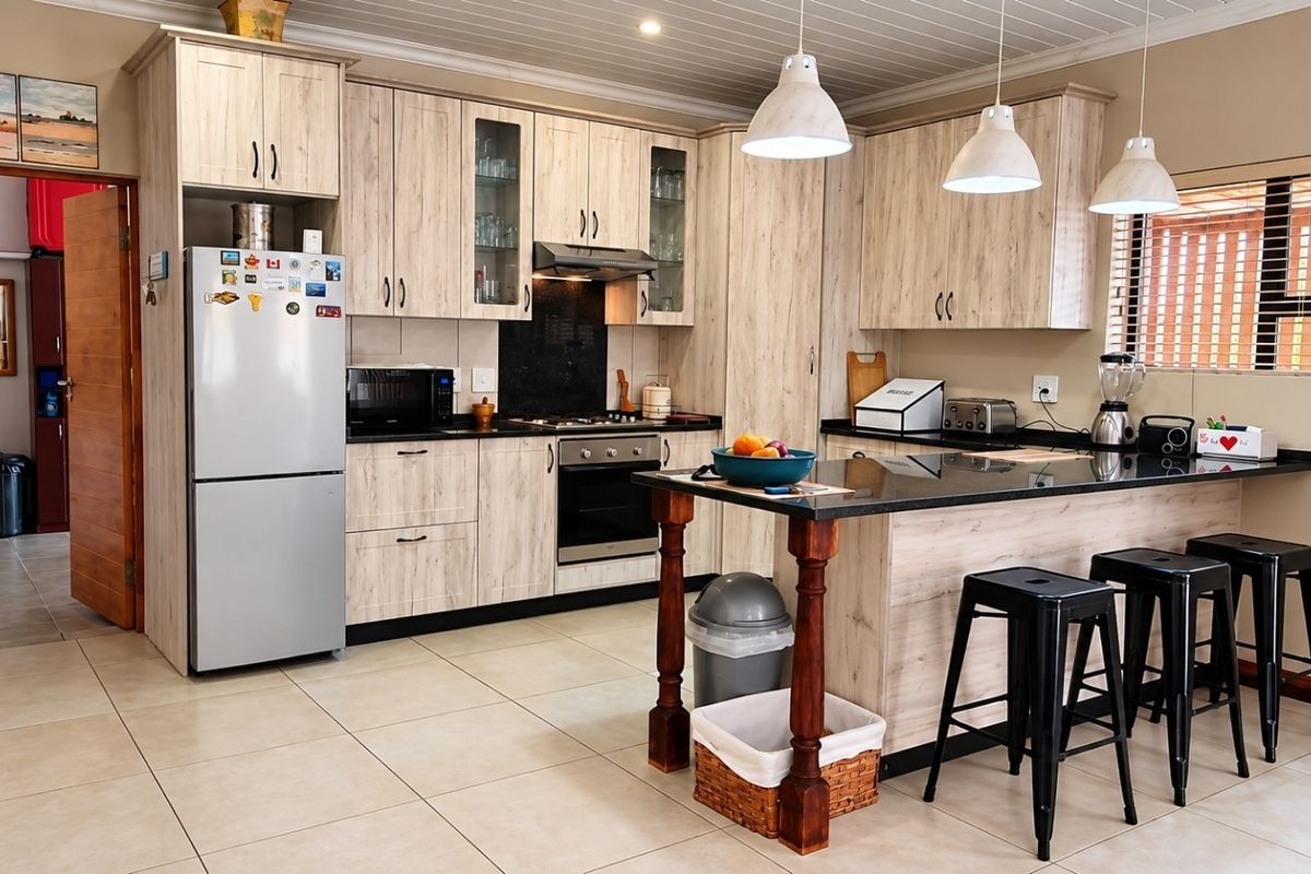 Modern kitchen featuring light wood-grain cabinetry, black granite countertops, a central island with breakfast bar, and tiled flooring.