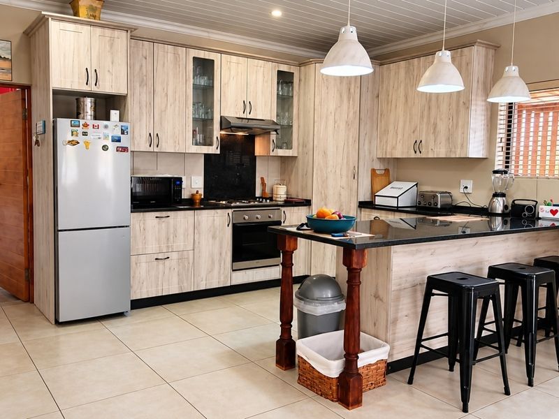 Modern kitchen featuring light wood-grain cabinetry, black granite countertops, a central island with breakfast bar, and tiled flooring.