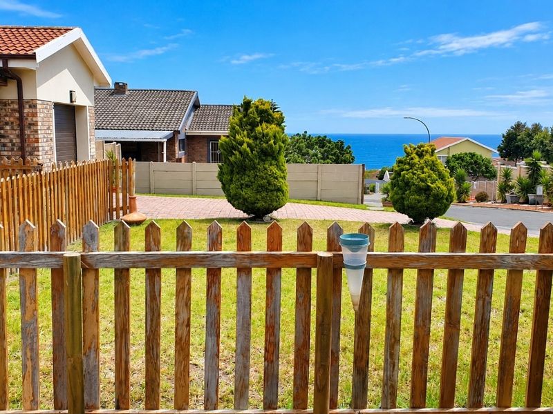 Front view of the property featuring a paved driveway, wooden picket fencing, and a clear view of the ocean in the distance.