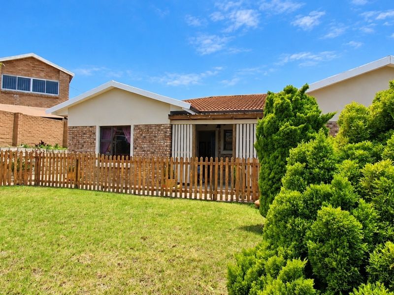 Front view of a single-story house featuring a brick facade, tiled roof, and a well-maintained front garden with a wooden picket fence.