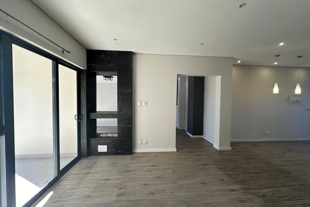 Spacious open-plan living area featuring modern laminate flooring, recessed downlights, and a striking black marble fireplace surround with access to an outdoor patio.