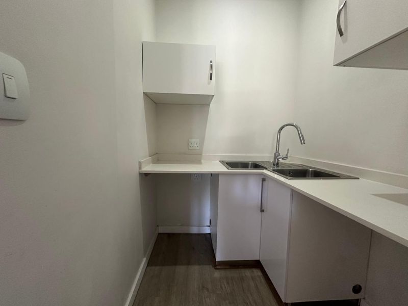 A clean and functional laundry area featuring built-in white cabinetry, laminate countertops, and a stainless steel sink with a modern mixer tap.