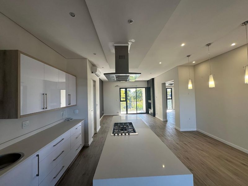 Spacious open-plan kitchen and living area featuring a large island with gas hob, modern cabinetry, recessed lighting, and wood-look laminate flooring.