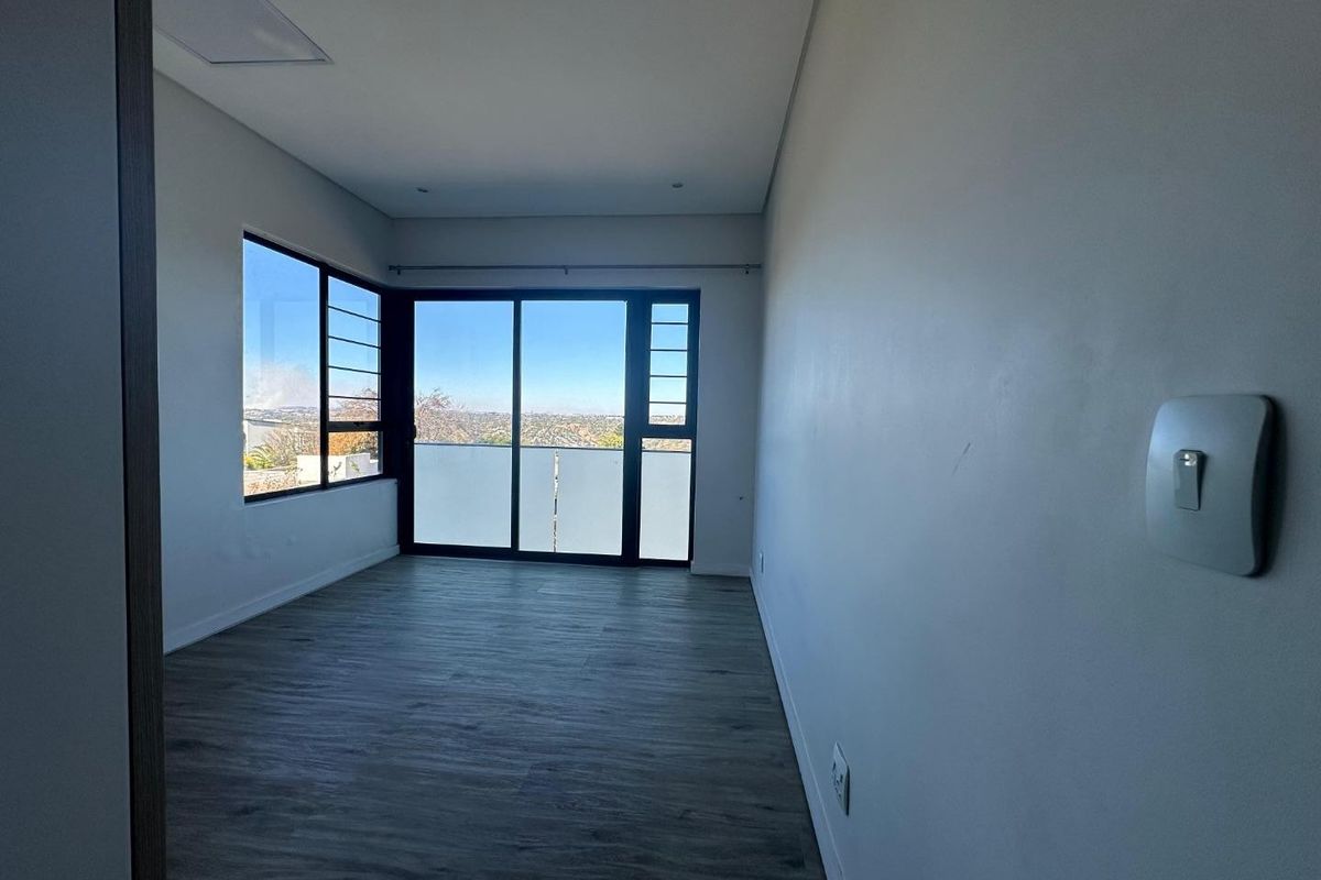 An empty bedroom featuring modern laminate flooring, recessed lighting, and a sliding glass door that opens to a balcony with scenic views.