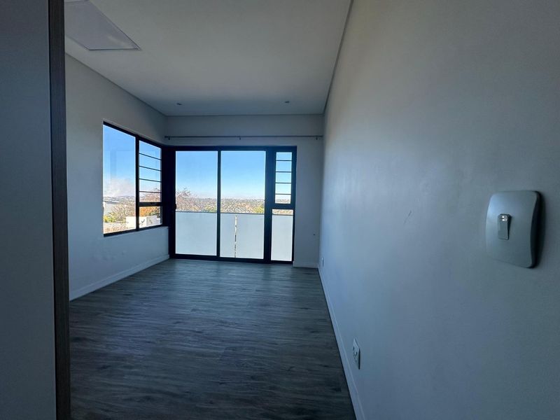 An empty bedroom featuring modern laminate flooring, recessed lighting, and a sliding glass door that opens to a balcony with scenic views.