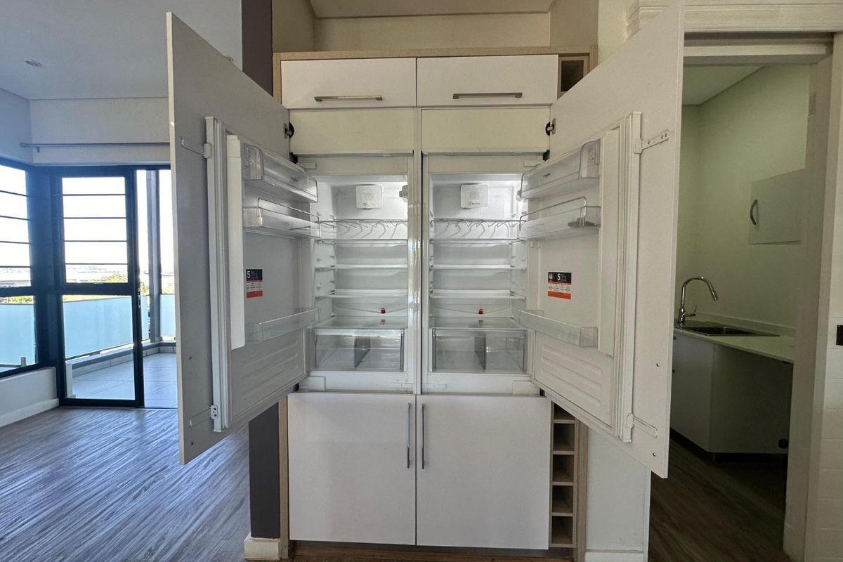 Modern kitchen area featuring an integrated double refrigerator unit, laminate flooring, and an adjacent scullery with a stainless steel sink.
