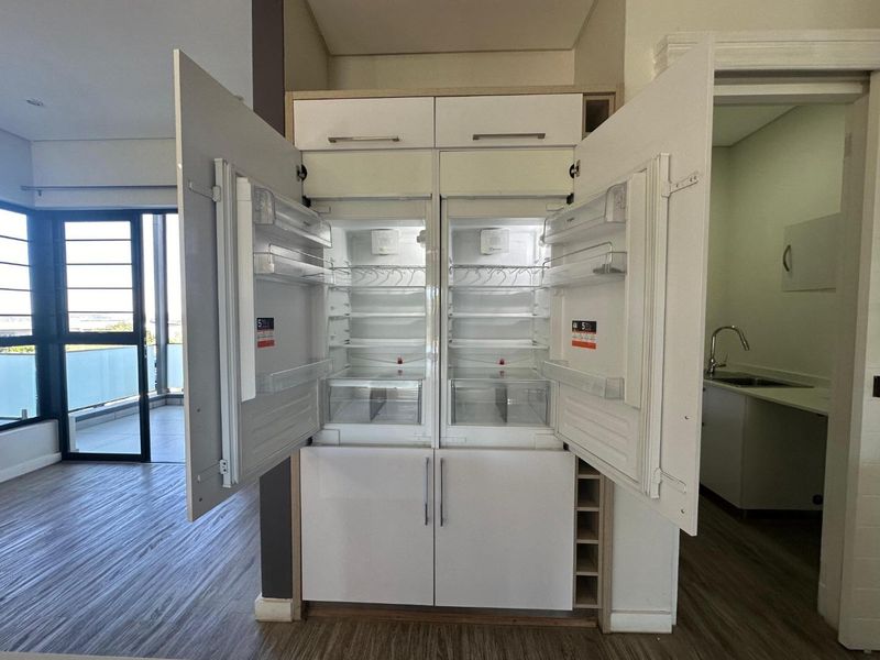 Modern kitchen area featuring an integrated double refrigerator unit, laminate flooring, and an adjacent scullery with a stainless steel sink.
