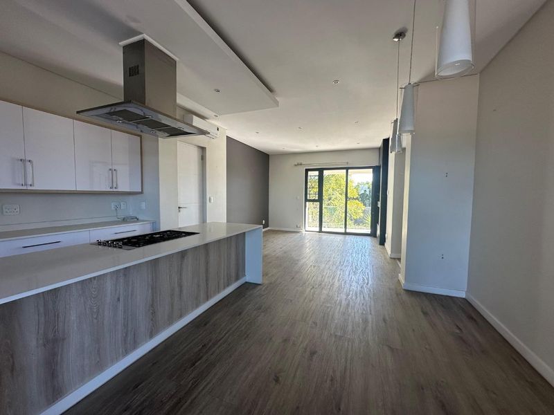 Modern open-plan kitchen and living area featuring sleek cabinetry, a central island with hob, laminate flooring, and large sliding doors leading to a balcony.
