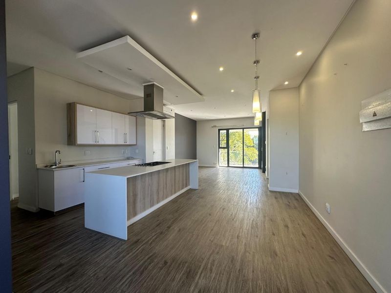 Spacious open-plan kitchen and living area featuring modern cabinetry, a central island with a hob, and sleek laminate flooring leading to a balcony.