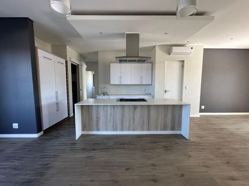 Modern open-plan kitchen featuring a central island with integrated cooktop, sleek cabinetry, and contemporary laminate flooring in a bright, spacious living area.