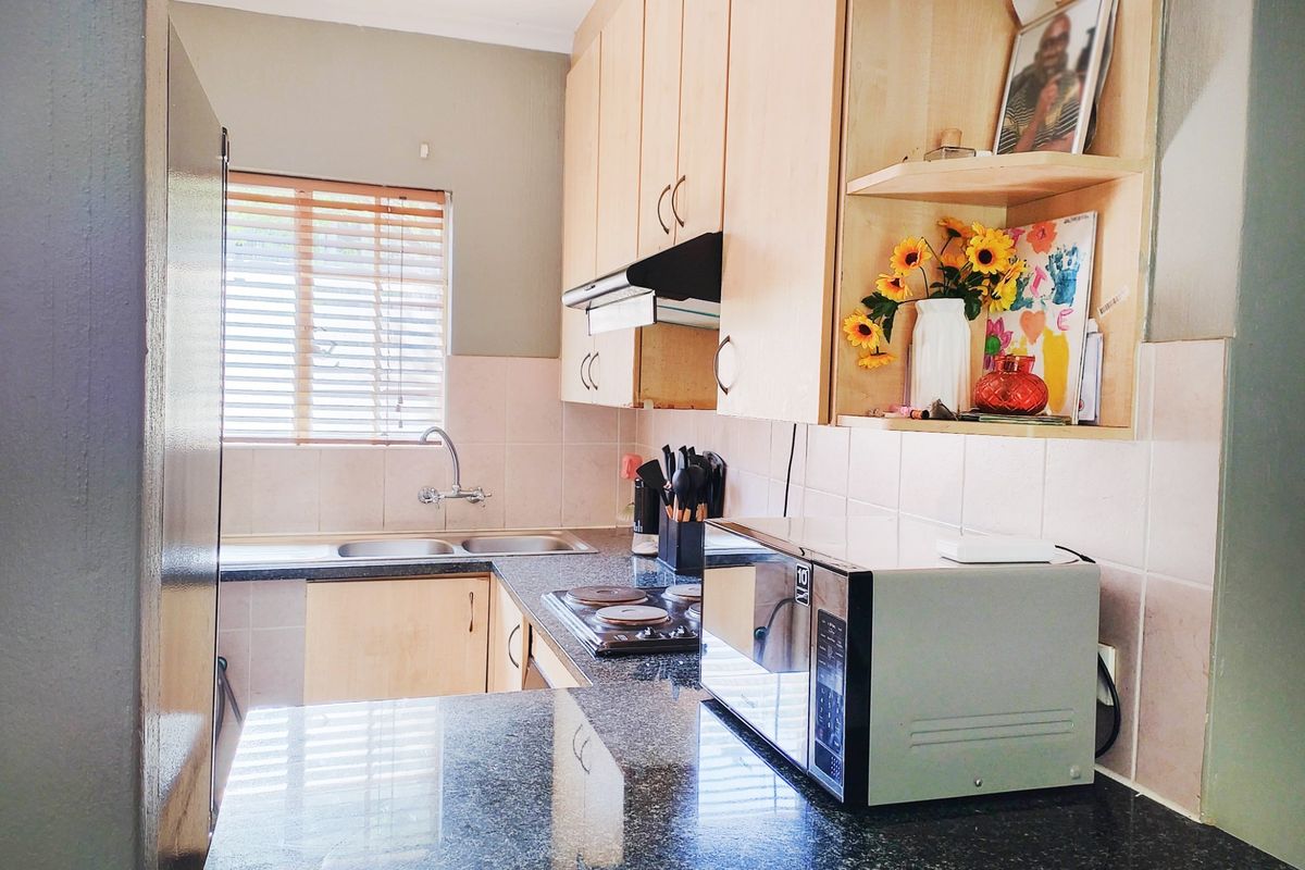 A functional kitchen featuring laminate cabinetry, granite countertops, a double basin sink, and an integrated electric hob with an extractor fan.