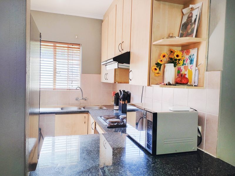 A functional kitchen featuring laminate cabinetry, granite countertops, a double basin sink, and an integrated electric hob with an extractor fan.