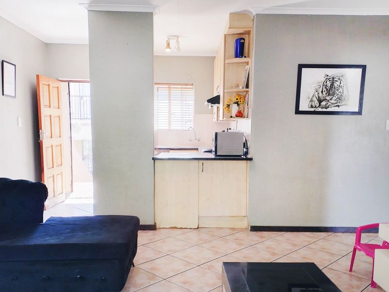Open plan living area featuring tiled flooring and a compact kitchen with built-in cabinetry, extractor fan, and sink, leading to an exterior entrance.