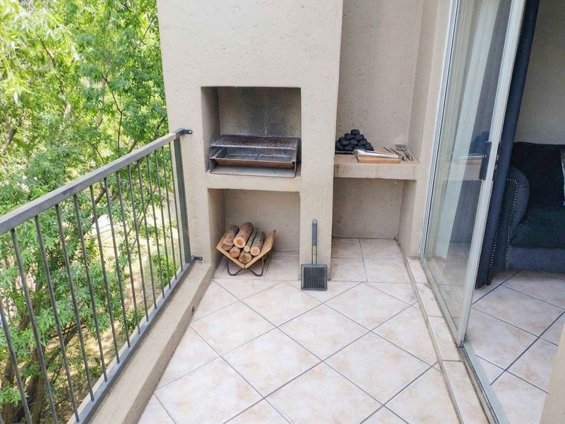 A covered balcony featuring a built-in braai, tiled flooring, and a metal balustrade, offering a functional outdoor entertainment space.