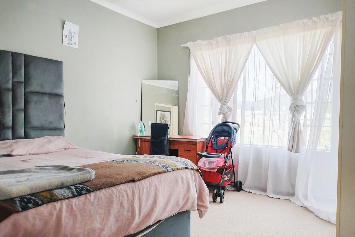 A bedroom featuring carpeted flooring and a large window with curtains, providing natural light to the space.