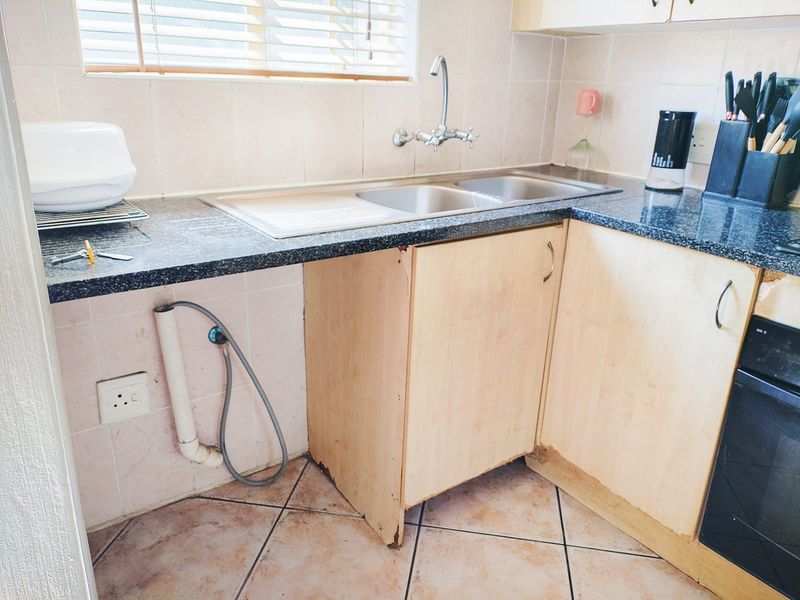 A functional kitchen area featuring granite countertops, a double bowl stainless steel sink, and built-in oven, showing signs of wear on the cabinetry.