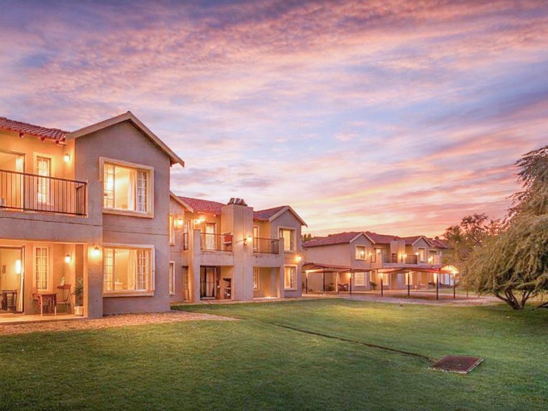 A scenic view of the apartment complex rear facade at sunset, featuring private balconies, ground-floor patios, and well-maintained communal lawn areas.