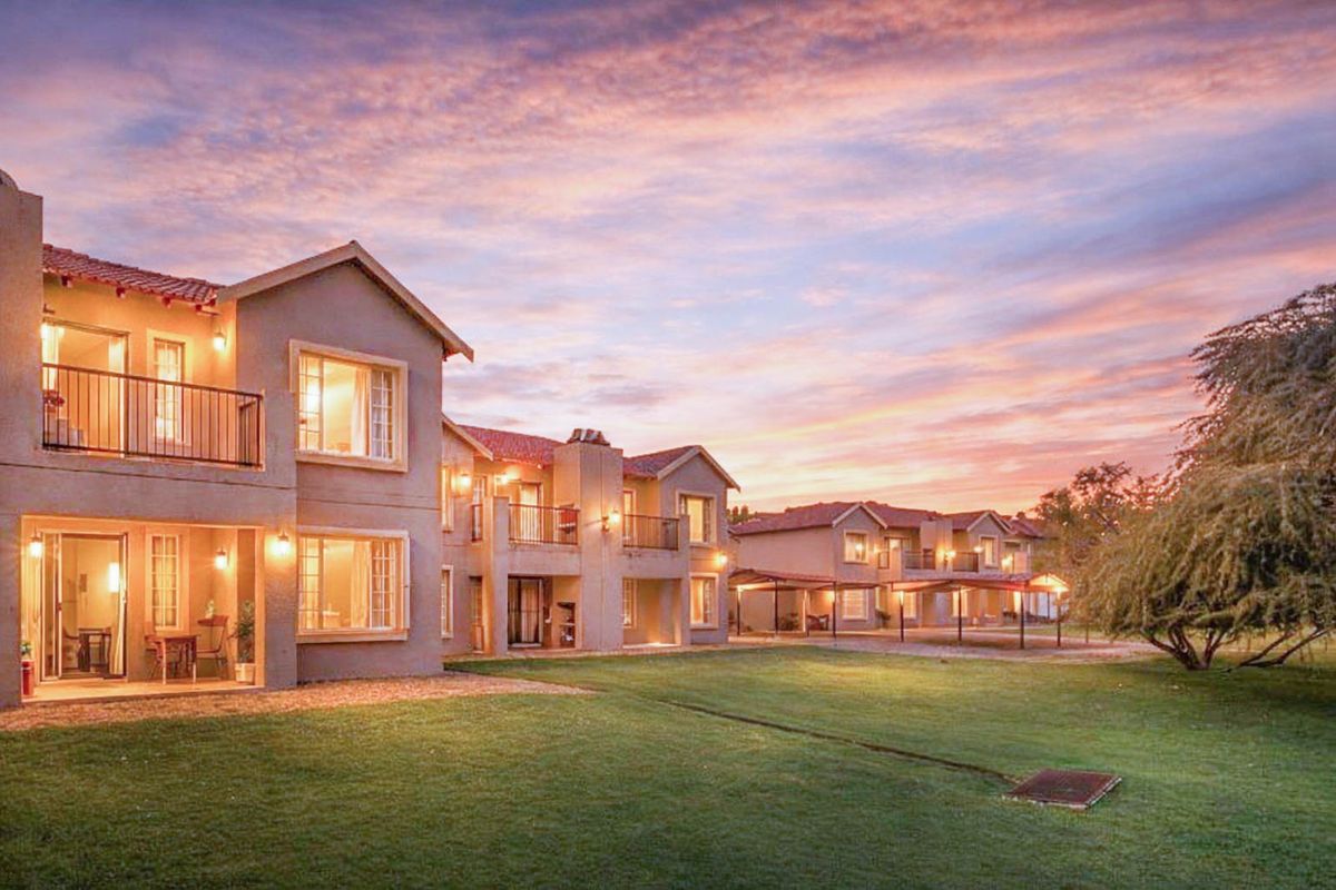 A scenic view of the apartment complex rear facade at sunset, featuring private balconies, ground-floor patios, and well-maintained communal lawn areas.