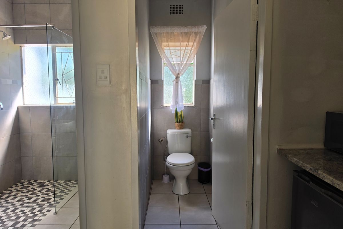 A functional bathroom featuring a toilet, tiled walls and flooring, and a glass-enclosed shower area with natural light.