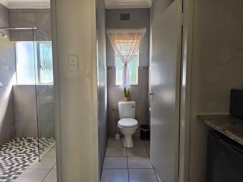 A functional bathroom featuring a toilet, tiled walls and flooring, and a glass-enclosed shower area with natural light.