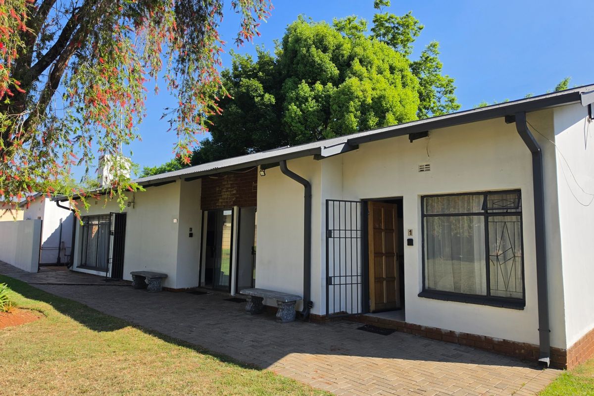 Rear exterior view of the guest house featuring a paved patio area, security gates, and direct access to multiple units.