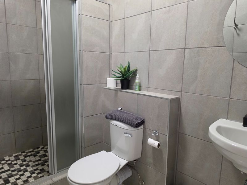 A modern bathroom featuring a shower enclosure, toilet, and wall-mounted basin with neutral grey wall tiling and a patterned floor.