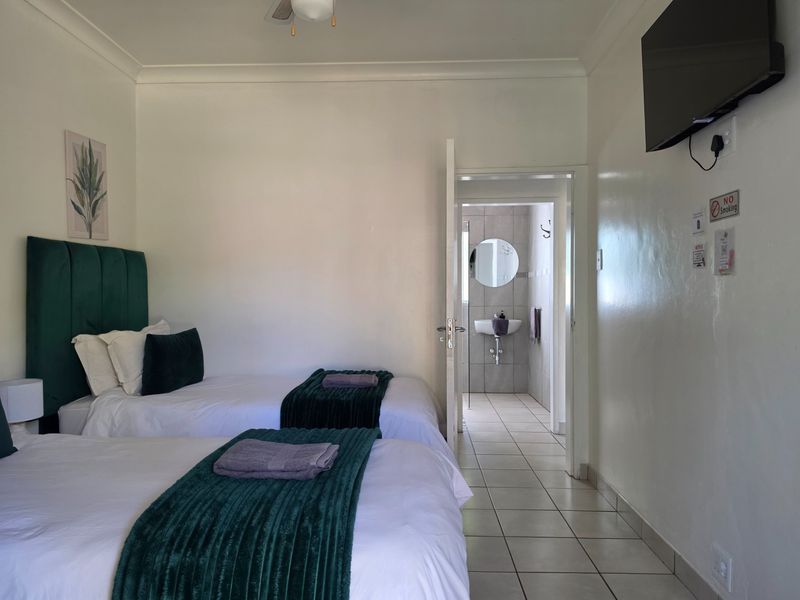A well-maintained bedroom featuring tiled flooring, a ceiling fan, and an en-suite bathroom with a wall-mounted television.